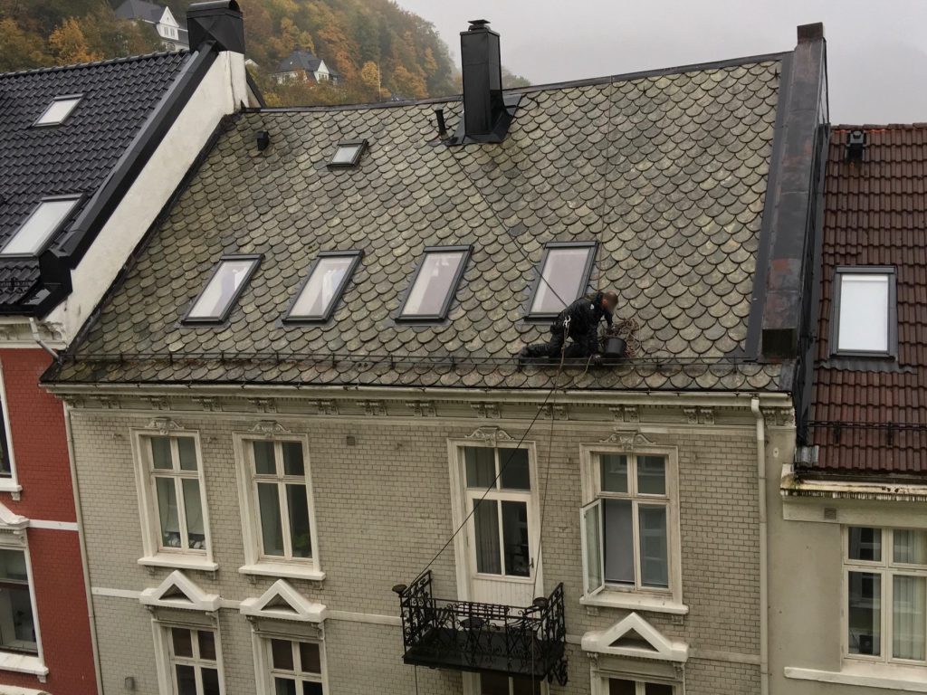 Technician cleaning a gutter from a steep roof
